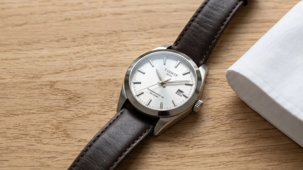 Tissot Gentleman Powermatic 80 Silicium white dial on brown leather strap on wood surface beside folded white cloth