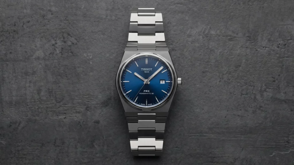 Tissot PRX Powermatic 80 blue dial on steel bracelet laid flat on dark grey textured surface