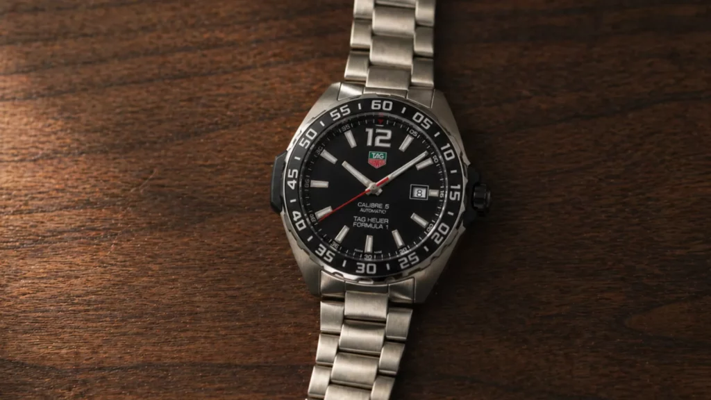 TAG Heuer Formula 1 Calibre 5 automatic black dial on steel bracelet laid on dark wood surface