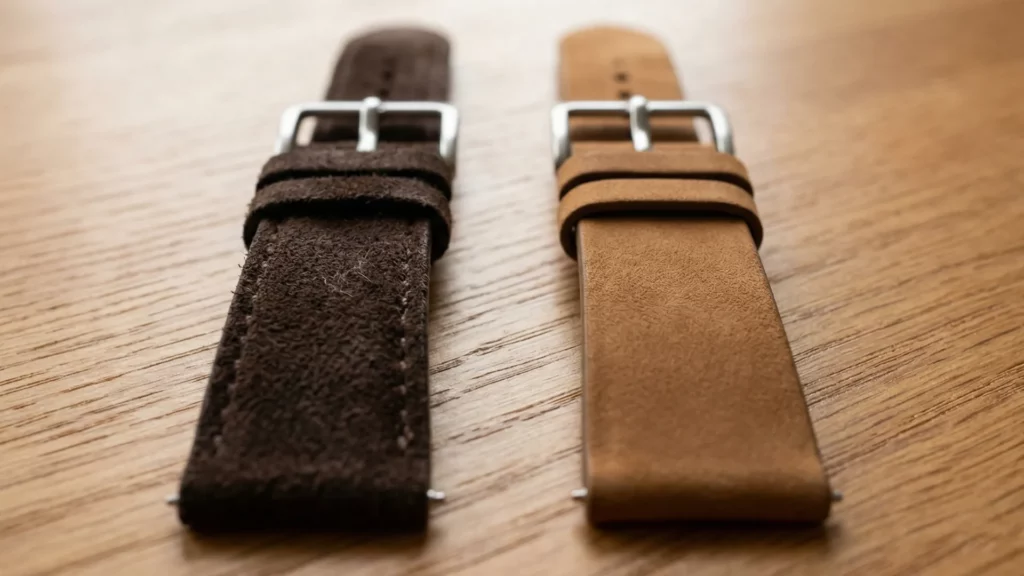 Dark brown suede and tan nubuck watch straps with silver buckles laid side by side on wood