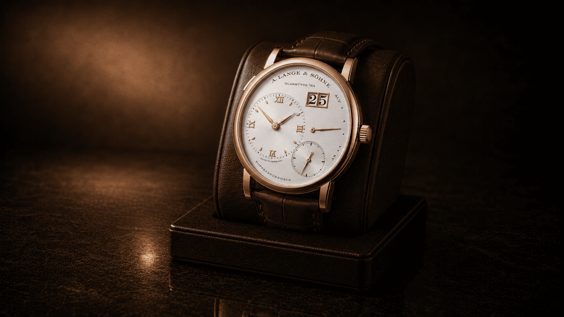 Rose-gold A. Lange & Söhne Lange 1 with silver dial and brown leather strap displayed on a black leather watch roll against a dark warm-toned background.