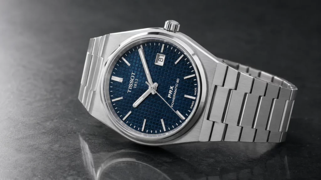 Tissot PRX Powermatic 80 stainless steel watch with a blue textured dial and integrated bracelet on a dark stone surface.