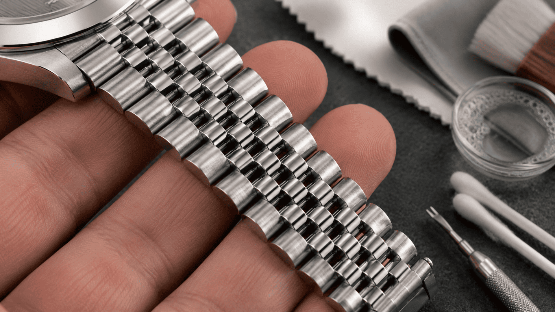 Caring for a stainless steel watch bracelet with a microfiber cloth and soft brush on a dark surface