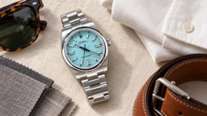 Turquoise dial luxury watch styled with cream shirt, cognac leather, and neutral wardrobe pieces in flat lay
