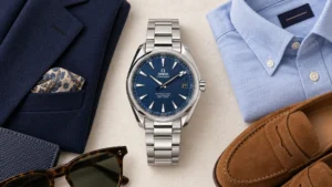 Omega Seamaster Aqua Terra blue dial beside a navy blazer, light blue shirt, tan suede loafers and sunglasses