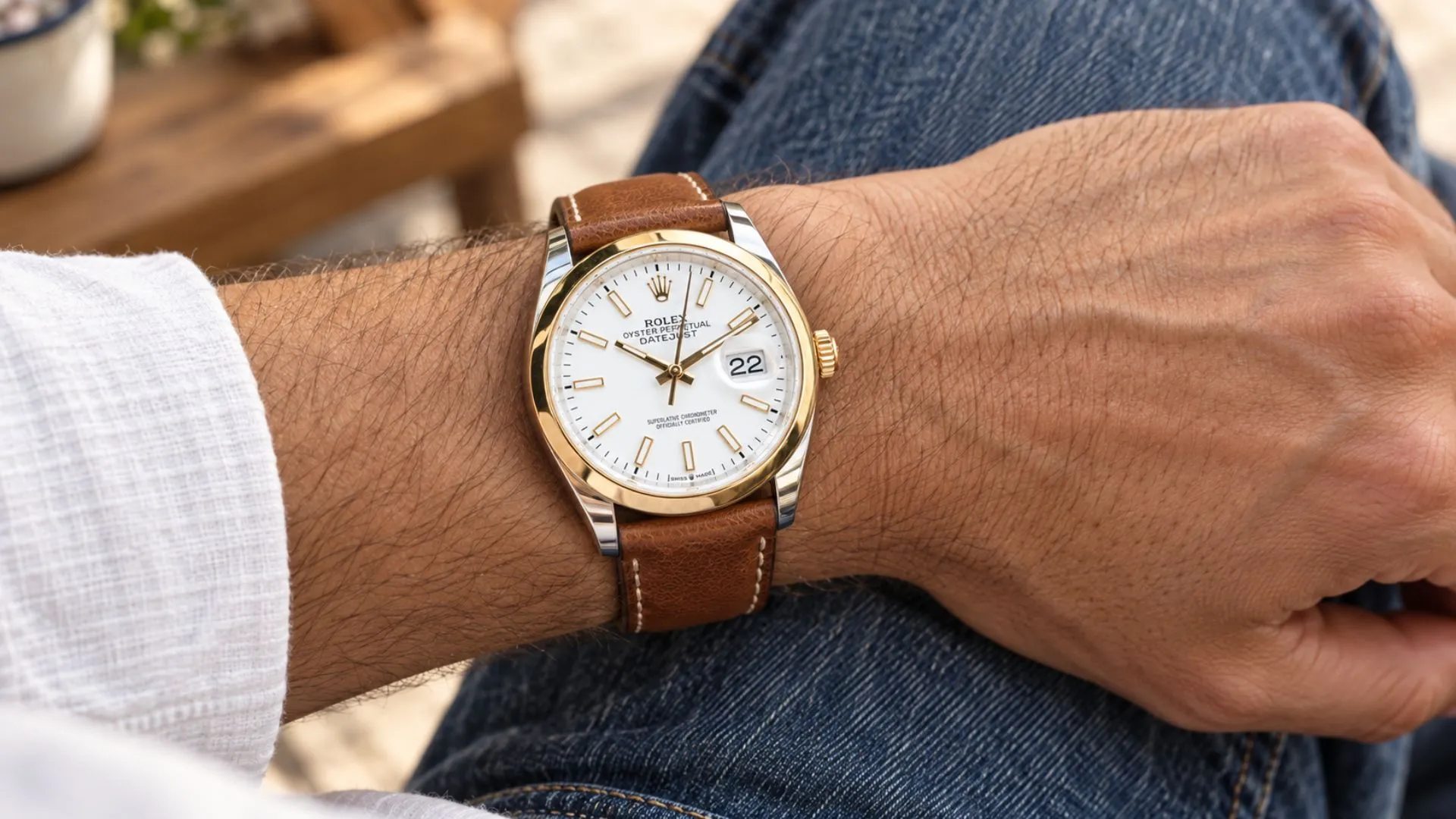 Two-tone Rolex Datejust with white dial on tan leather strap worn on wrist with denim and linen shirt